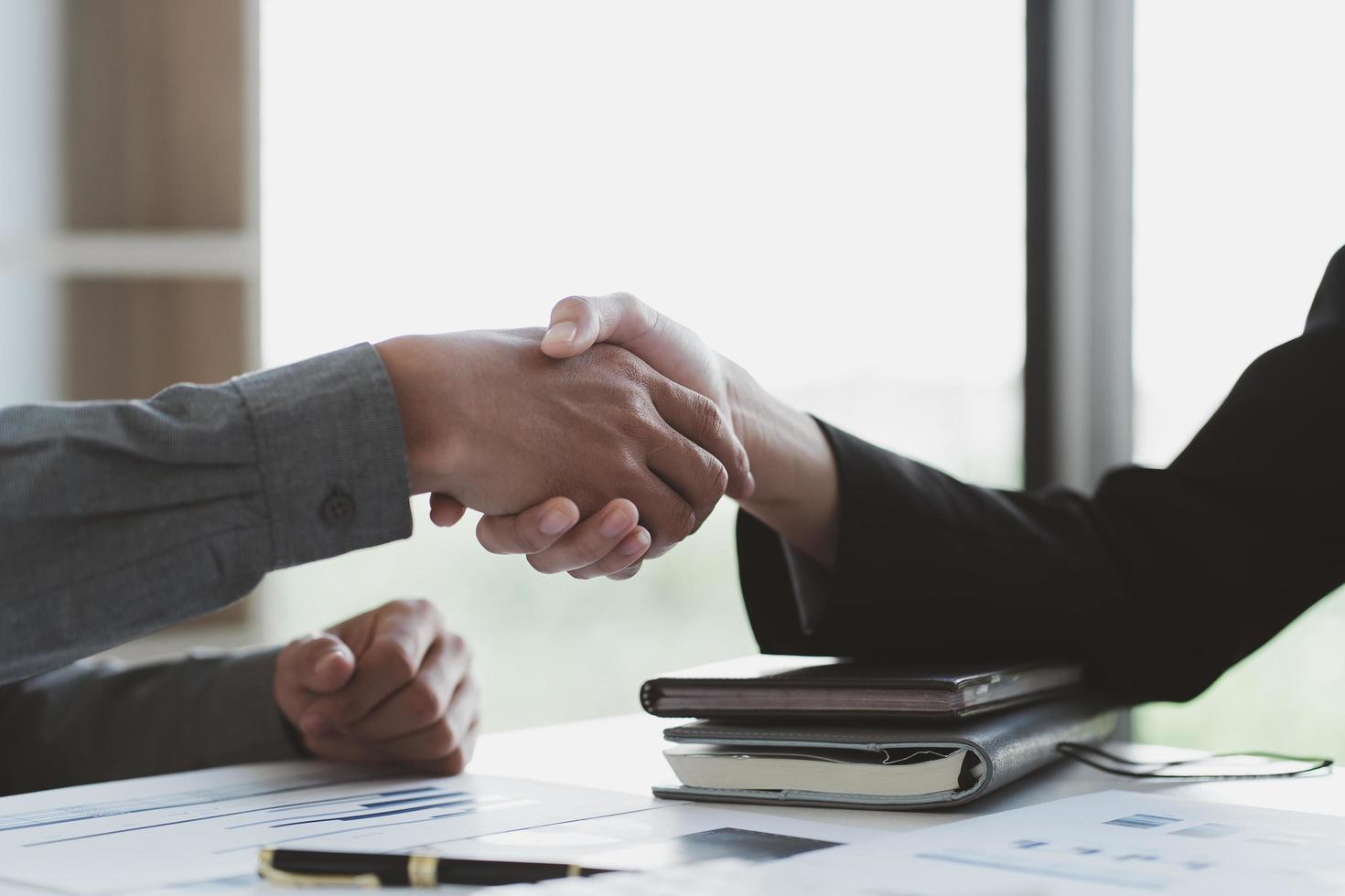 Close up of female and male shaking hands, businessman and businesswoman handshaking above office table with charts graphs after successful negotiations, partners concluding contract, top view photo