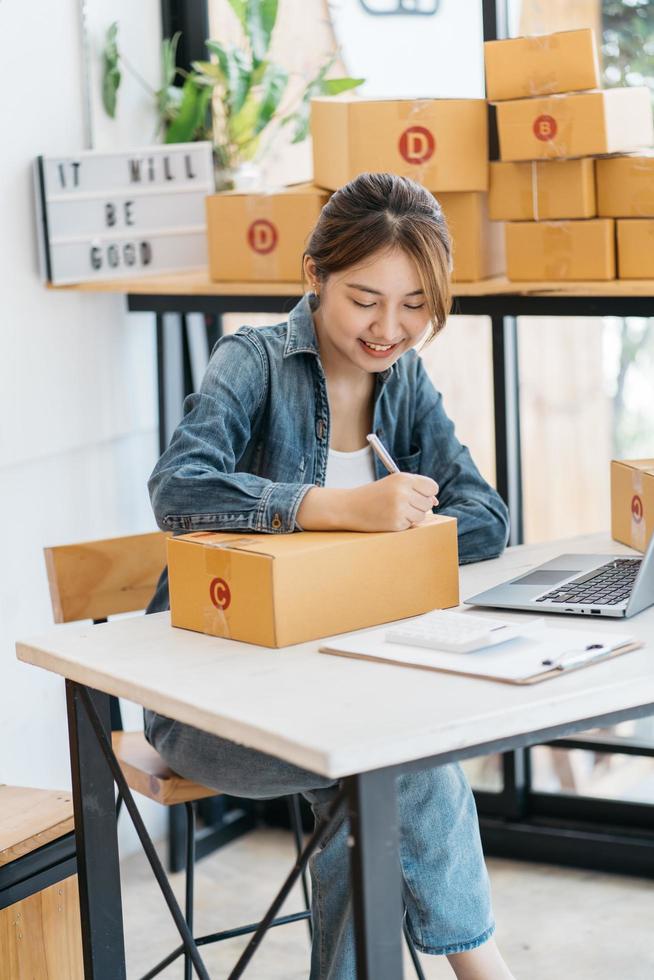 empresaria asiática está empacando productos en la caja en el lugar de trabajo de su casa. el propietario de un negocio adolescente trabaja en casa, muchas cosas que hacer hoy en casa. poner en marcha el concepto de sme. foto