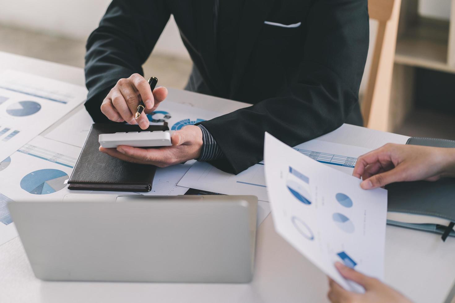 Close up of businessman or accountant hand holding pen working on calculator to calculate business data, accountancy document and laptop computer at office, business concept photo
