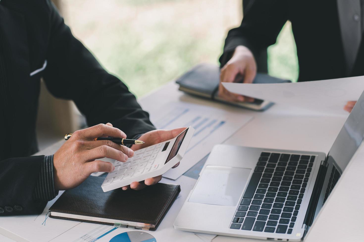 Cerca de la mano del empresario o contador que sostiene la pluma trabajando en la calculadora para calcular datos comerciales, documentos contables y computadora portátil en la oficina, concepto de negocio foto