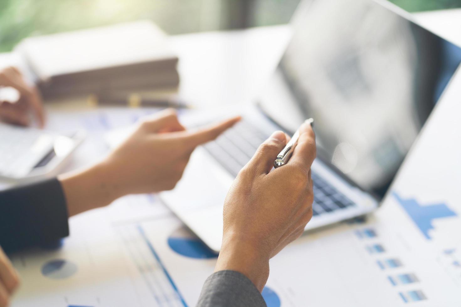 Close up of hands of two men and woman wearing casual clothes working with graphs at a white table and making notes. Locked down real time close up shot photo