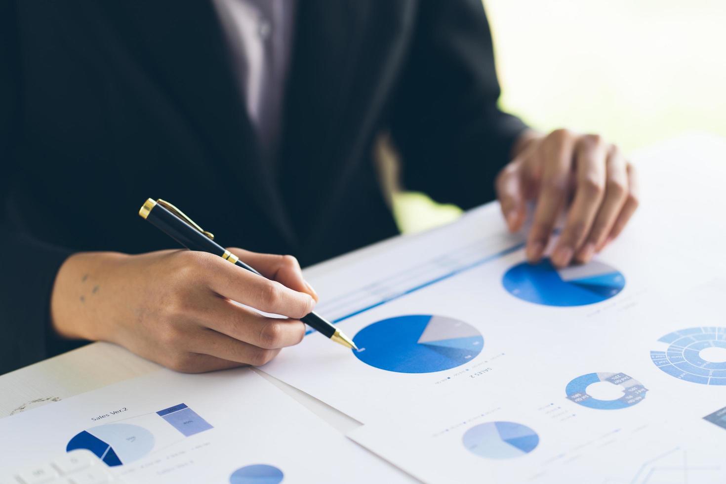 Close up of businesswoman holding a pen and pointing at the information sheet on his desk, reading the company's financials to make a financial plan. Financial concept. photo