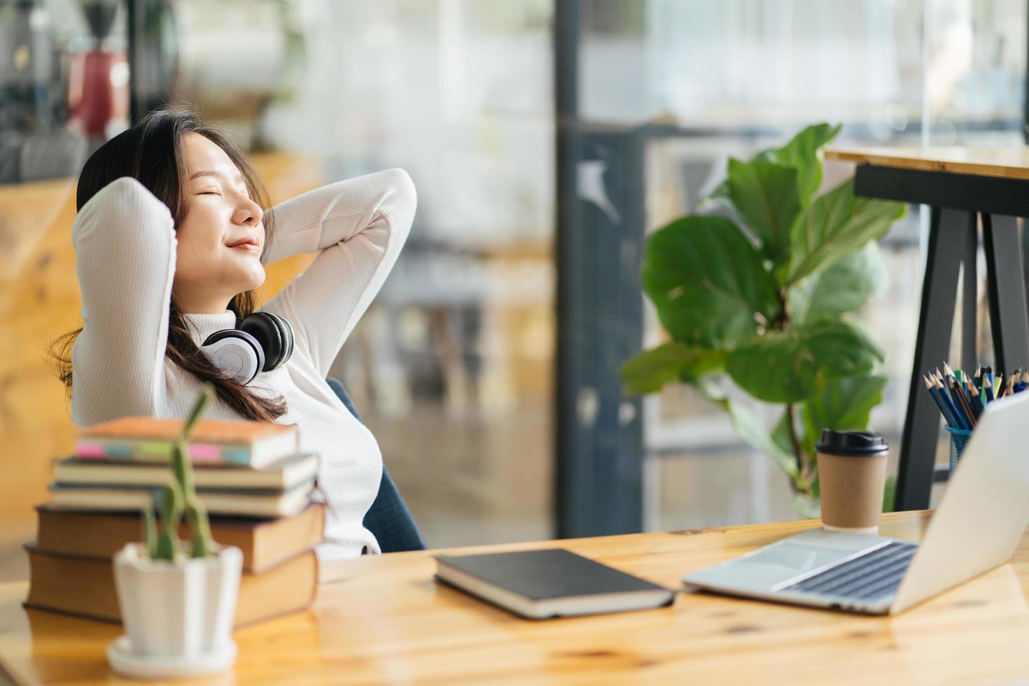 Happy calm asian girl student relaxing holding hands behind finished study work breathing fresh air sit at home office desk feel stress relief stretching doing exercise dreaming enjoy peace of mind photo