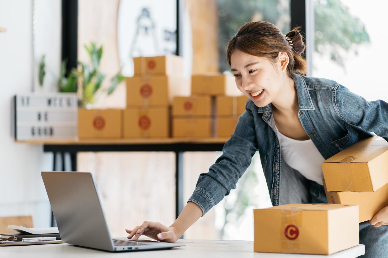 empresaria asiática está empacando productos en la caja en el lugar de trabajo de su casa. el propietario de un negocio adolescente trabaja en casa, muchas cosas que hacer hoy en casa. poner en marcha el concepto de sme. foto