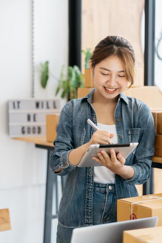 trabajador en almacén marcando casillas usando tableta digital. poner en marcha un pequeño empresario pyme o una mujer independiente que trabaja en el concepto de hogar, joven propietario de una pequeña empresa asiática, marketing en línea. foto