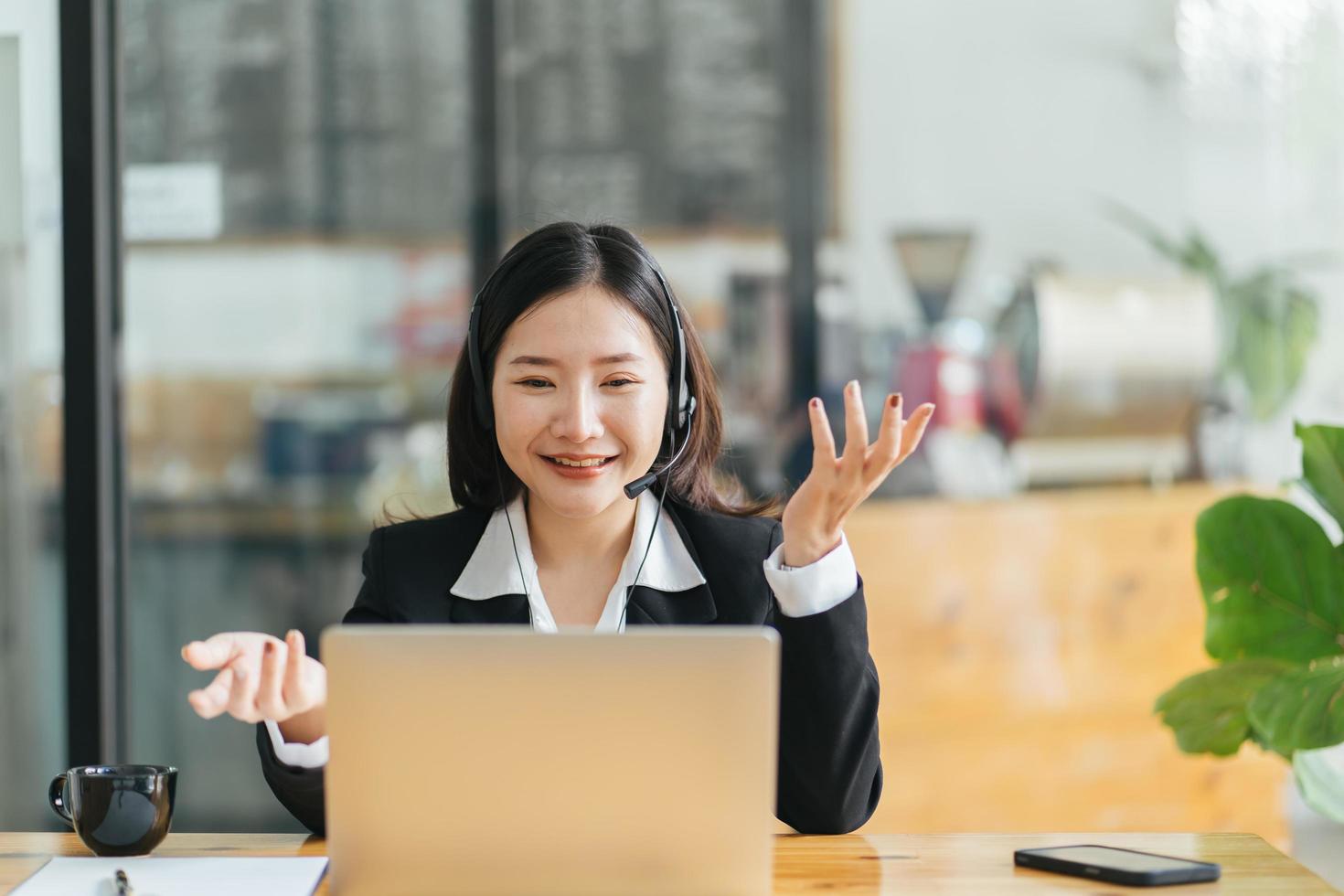 Side view head shot smiling asian lady freelancer wearing headset, communicating with client via video computer call. Millennial pleasant professional female tutor giving online language class. photo