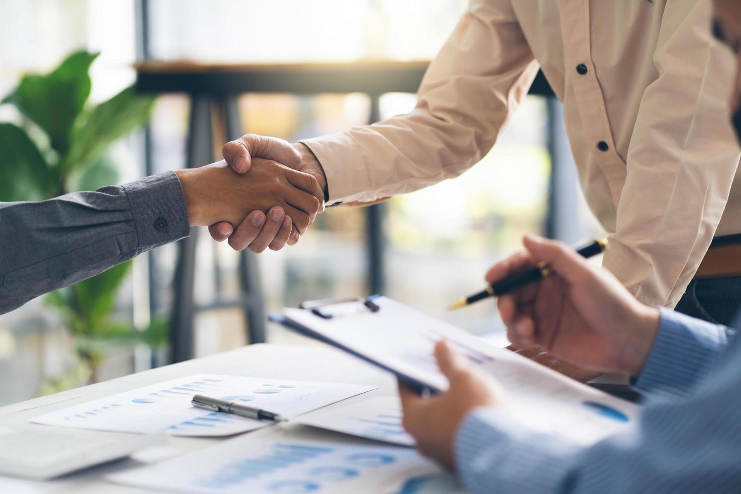 Entrepreneurs collaboration deal shaking hands in a modern office and financial paper graph on desk. photo