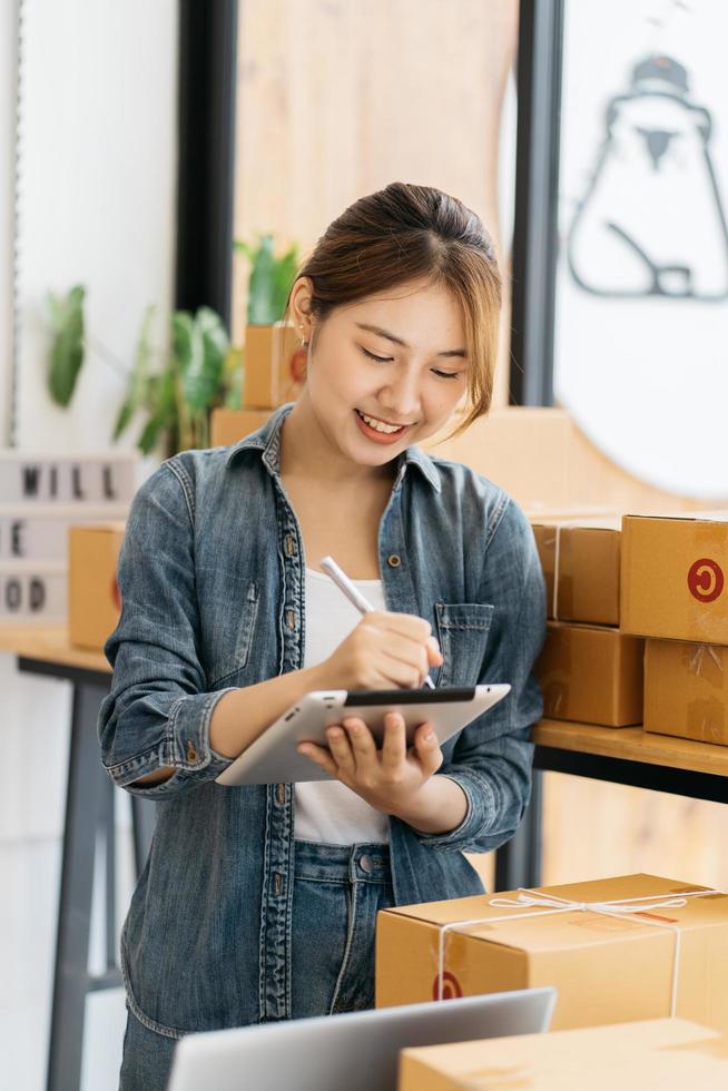 Worker In Warehouse Checking Boxes Using Digital Tablet.Start up small business entrepreneur SME or freelance woman working at home concept, Young Asian small business owner,online marketing. photo