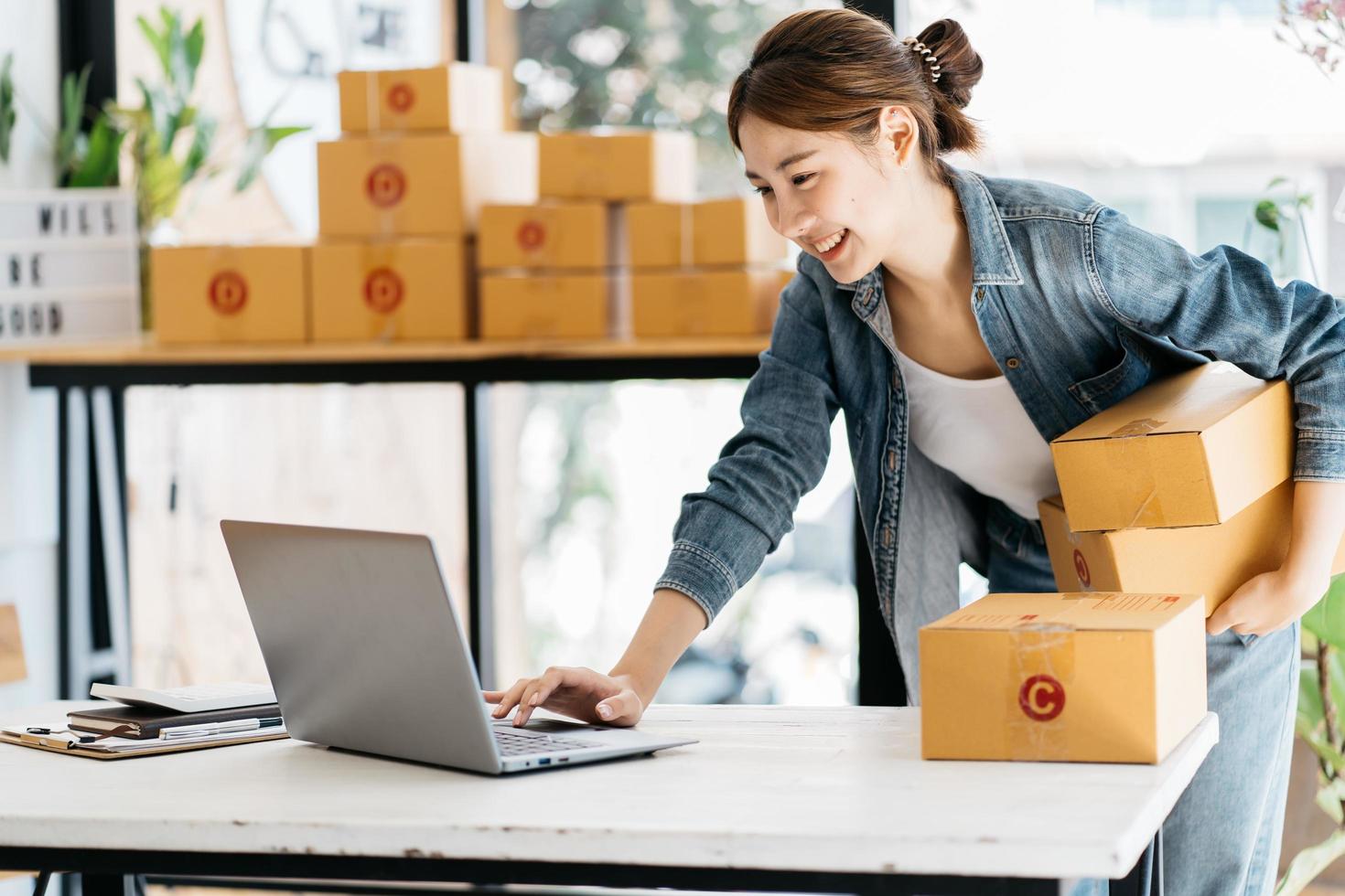 pequeña empresa emprendedora de mujeres asiáticas jóvenes que trabajan con una computadora portátil para comprar en línea en casa, alegre y feliz con una caja para empacar en casa, un negocio propio que comienza un negocio en línea foto