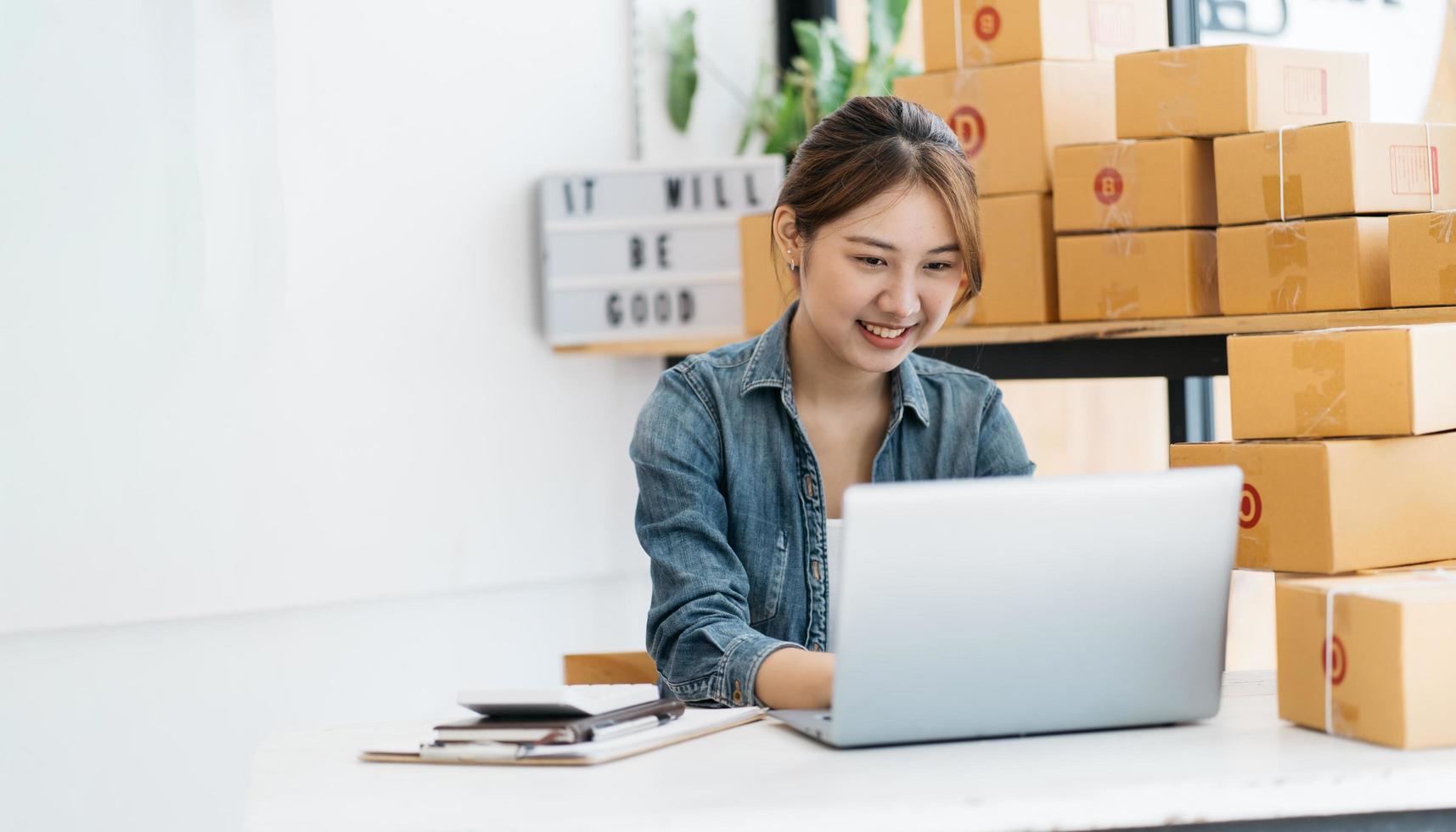 pequeña empresa emprendedora de mujeres asiáticas jóvenes que trabajan con una computadora portátil para comprar en línea en casa, alegre y feliz con una caja para empacar en casa, un negocio propio que comienza un negocio en línea foto
