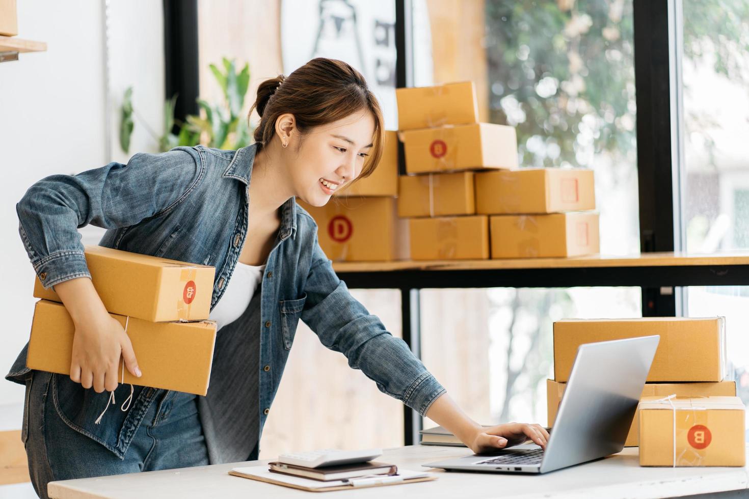 pequeña empresa emprendedora de mujeres asiáticas jóvenes que trabajan con una computadora portátil para comprar en línea en casa, alegre y feliz con una caja para empacar en casa, un negocio propio que comienza un negocio en línea foto