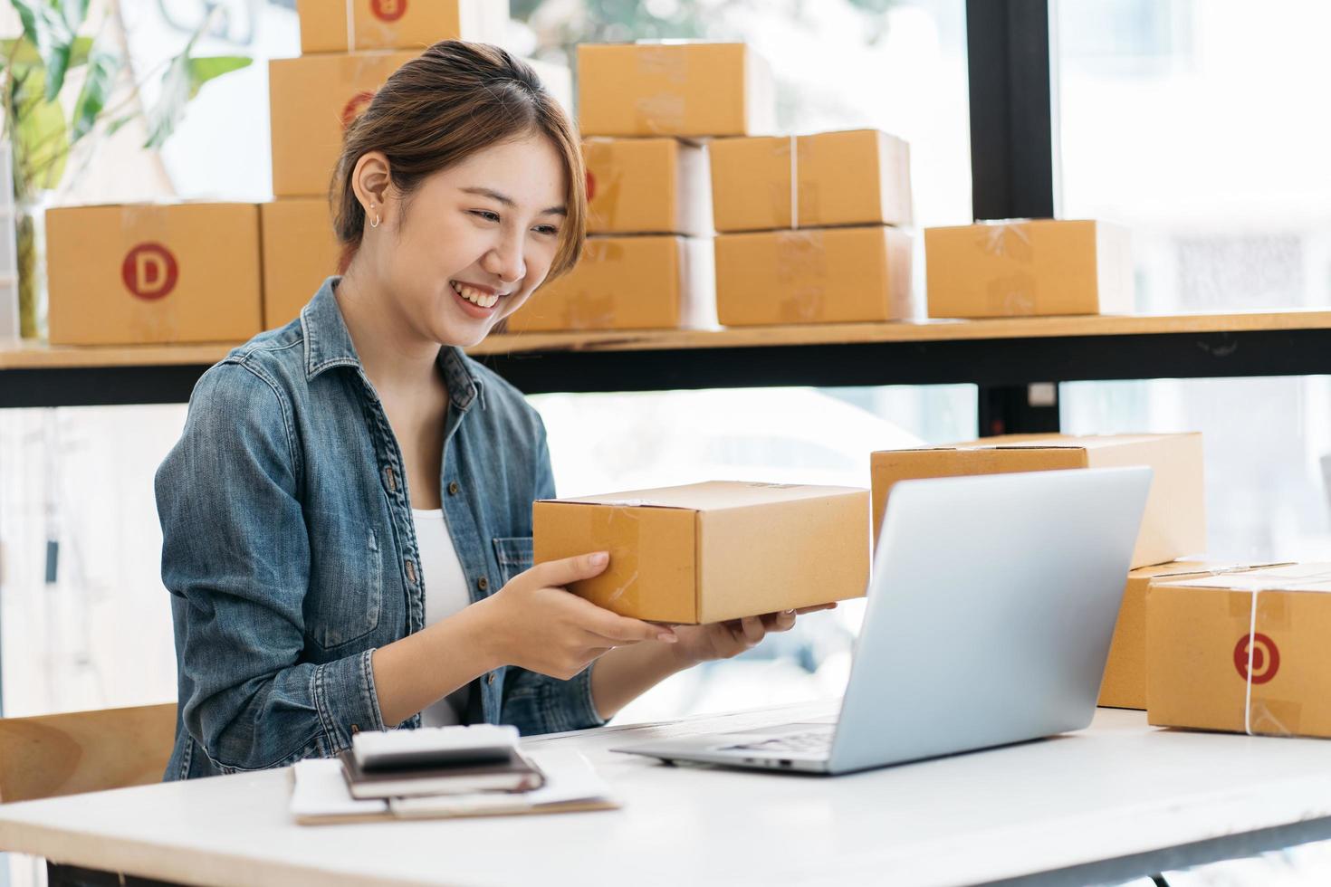 pequeña empresa emprendedora de mujeres asiáticas jóvenes que trabajan con una computadora portátil para comprar en línea en casa, alegre y feliz con una caja para empacar en casa, un negocio propio que comienza un negocio en línea foto