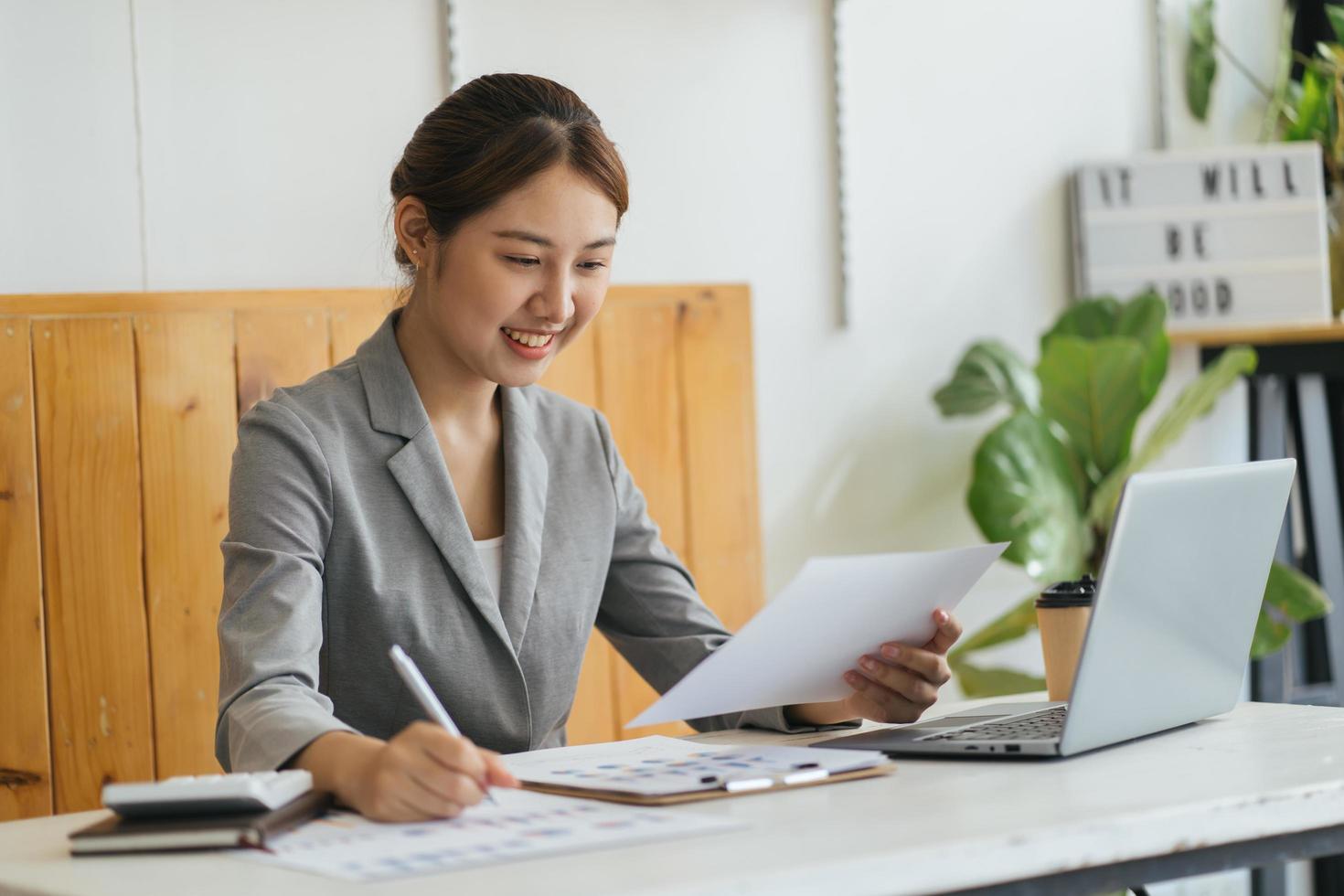 Happy young Asian woman sitting and using laptop in living room by working from home concept photo