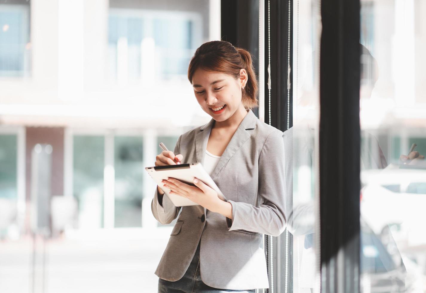 Attractive businesswoman using a digital tablet while standing in front of windows in an office building overlooking the city photo