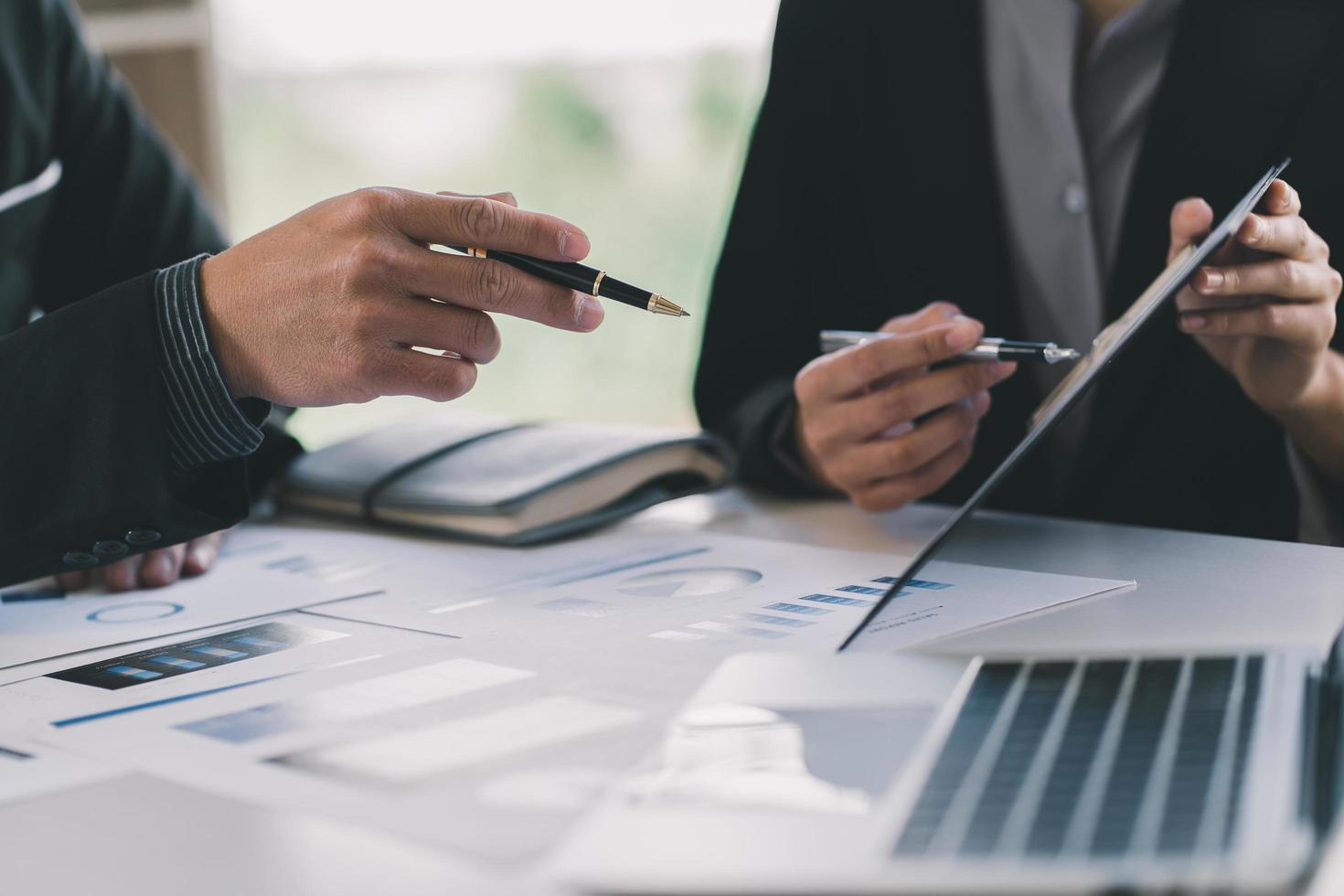 Cerca de la mano del empresario o contador que sostiene la pluma trabajando en la calculadora para calcular datos comerciales, documentos contables y computadora portátil en la oficina, concepto de negocio foto