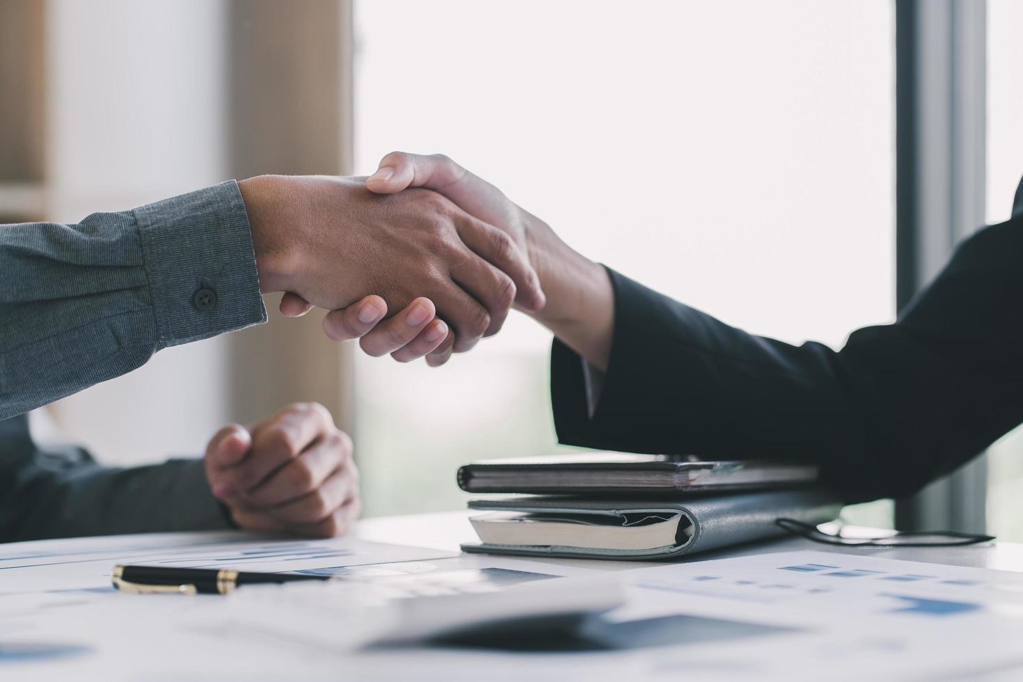 Close up of female and male shaking hands, businessman and businesswoman handshaking above office table with charts graphs after successful negotiations, partners concluding contract, top view photo