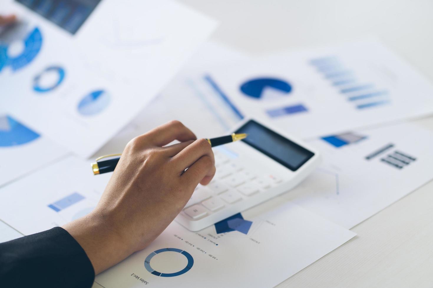 attractive business woman working on table with laptop and caculator and holding pen point on graph on paper to analyse business and marketing. photo