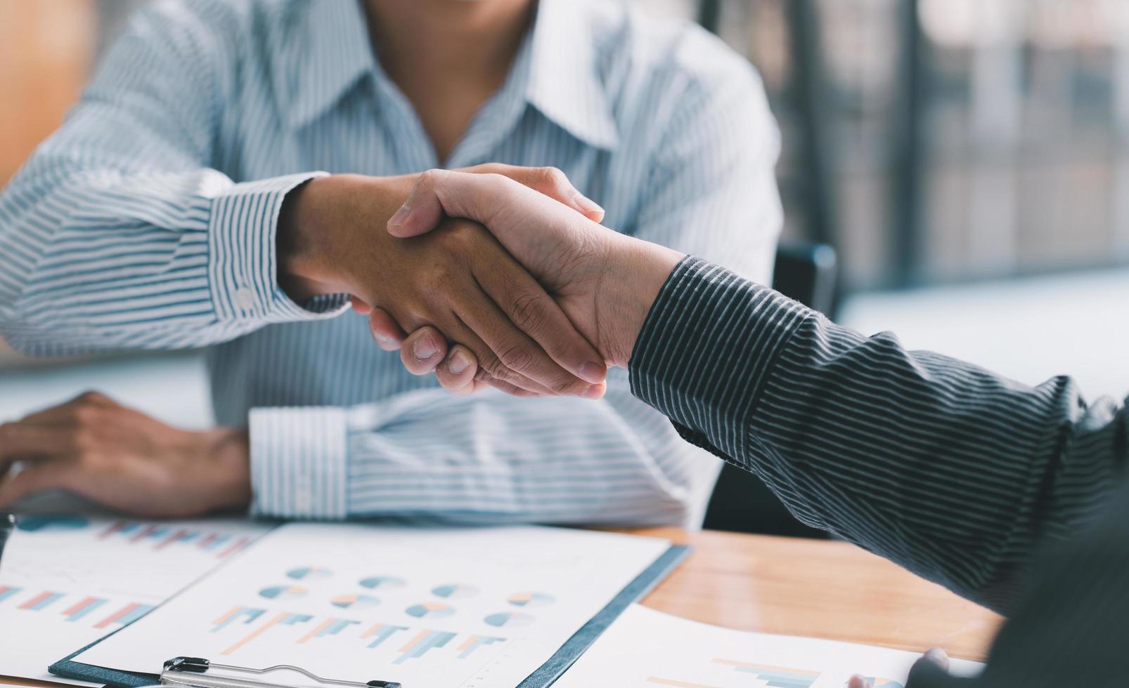 businesspeople are shaking their hands after signing a contract, while standing together in a sunny modern office, close-up. Business communication, handshake, and marketing concept photo