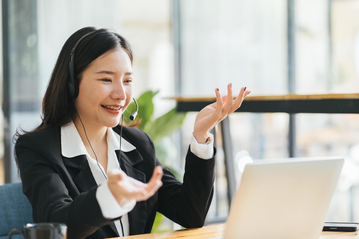 vista lateral tiro en la cabeza sonriente mujer asiática independiente con auriculares, comunicándose con el cliente a través de una videollamada. tutora profesional milenaria y agradable que da clases de idiomas en línea. foto