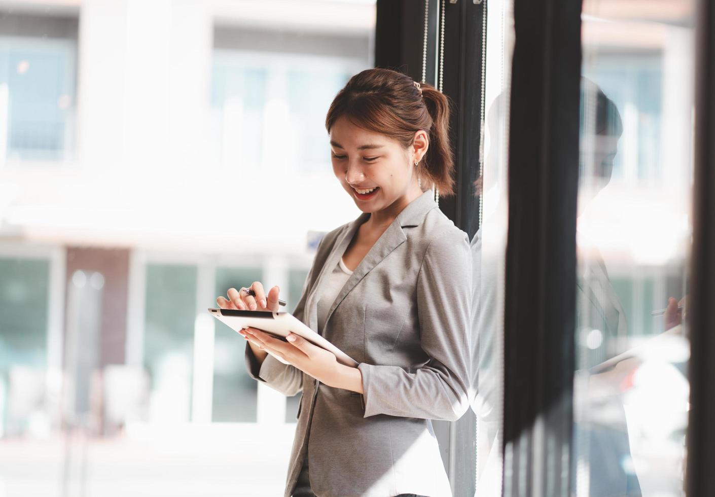 Attractive businesswoman using a digital tablet while standing in front of windows in an office building overlooking the city photo