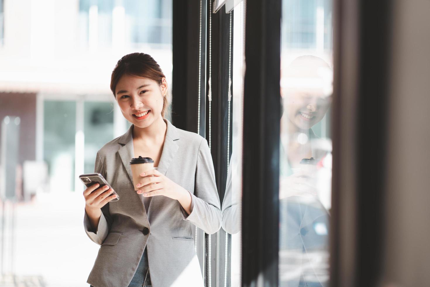 Smiling woman in casuals standing in office. Businesswoman with mobile phone in hand looking at camera. photo