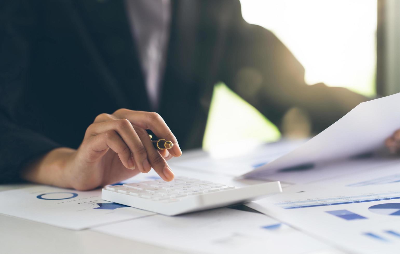 mujer de negocios atractiva que trabaja en la mesa con una computadora portátil y una caculadora y sostiene un punto de pluma en un gráfico en papel para analizar negocios y marketing. foto