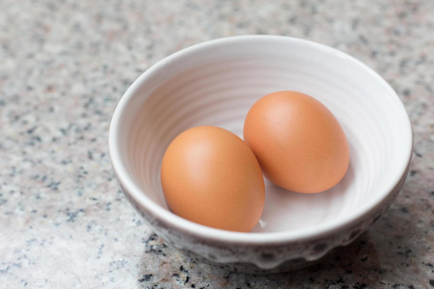 dos huevos frescos de color marrón claro en una taza sobre una mesa de granito. foto