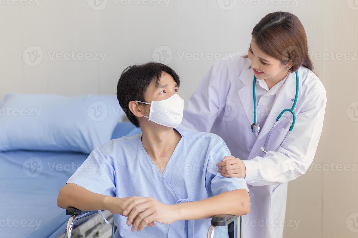 Asian doctor woman talking with a man patient who wear face mask about his health symptom while he sit on wheelchair at hospital. photo
