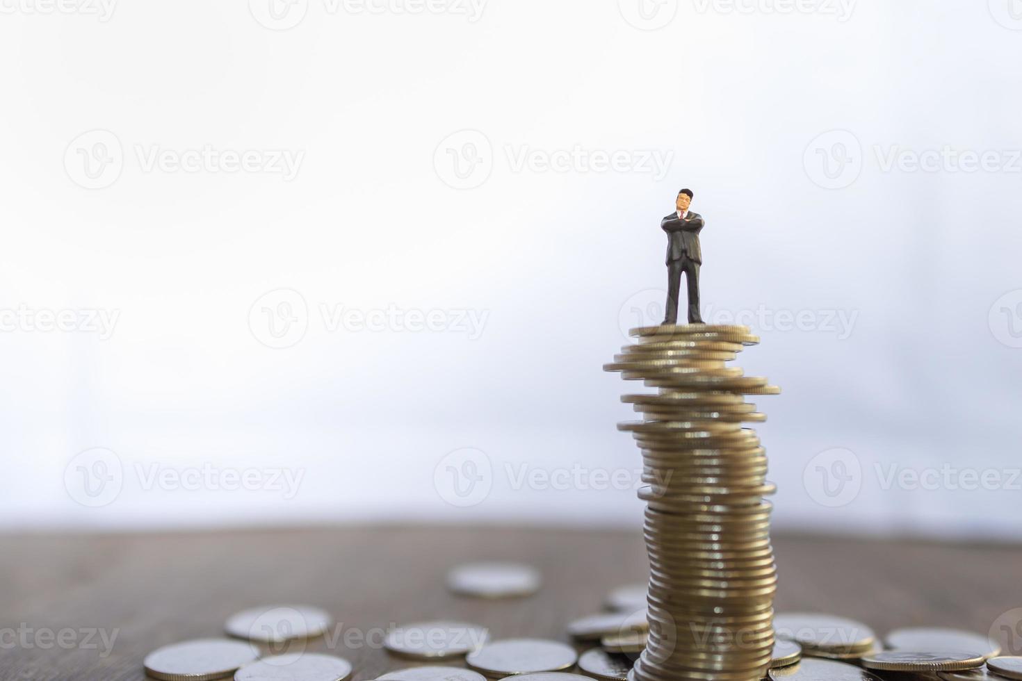 Business, Risk, Investment and Saving Concept.  Close up of businessman miniature people figure standing on top of unstable stack of coins with copy space. photo