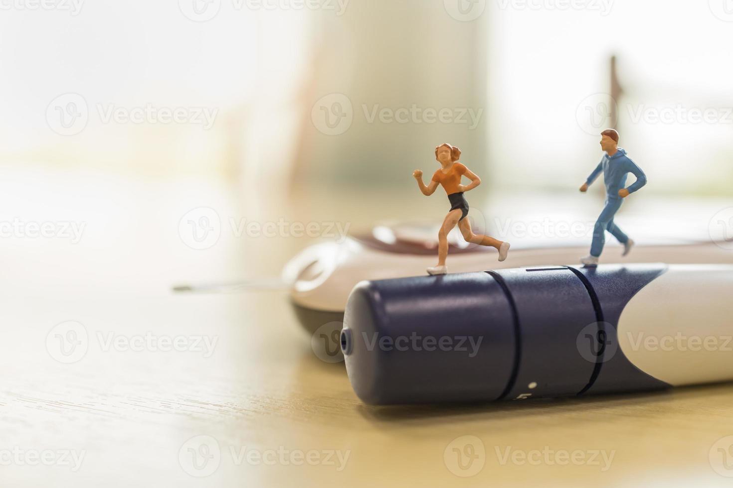 Medicine, diabetes, glycemia, health care and people concept - close up of woman and man runner miniature figure running on lancet with Glucose meter on wooden table. photo