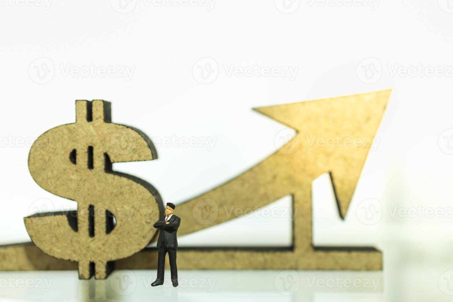 negocios, dinero, concepto de crecimiento financiero. primer plano de la figura de la mniatura del hombre de negocios personas de pie con signo de dólar de madera y flecha con espacio de copia. foto