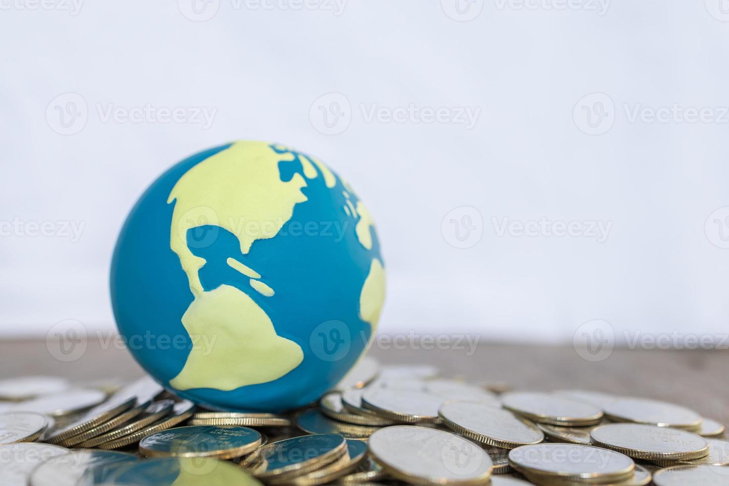 Global Business and Financial Concept. Close up of world mini ball on pile of coins on wooden table and copy space. photo