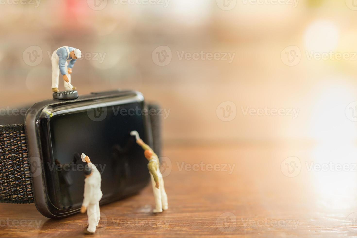 Technology, Time Concept. Close up of group of worker and painter miniature figure people clean and paint on smart watch on wooden table and copy space. photo