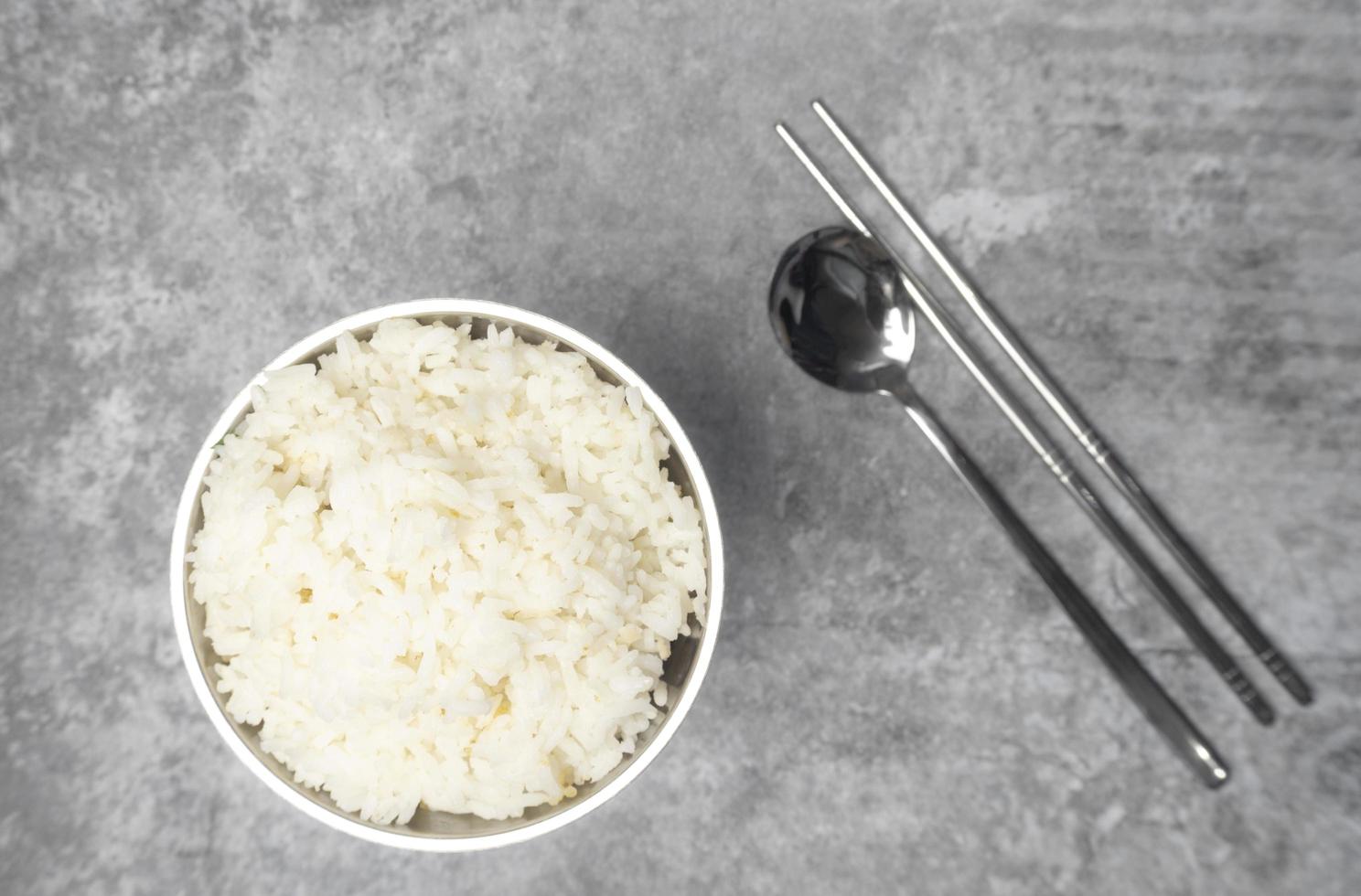 Top view steamed rice in a stainless bowl with spoon and chopsticks on the gray concrete table photo