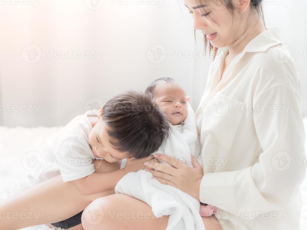 A beautiful Asian woman holds her newborn daughter and her son hugs his sister with love as well photo