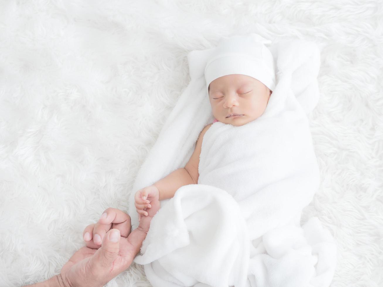 Newborn baby girl sleeps warmly on the white cloth and touched her father's hand with love photo