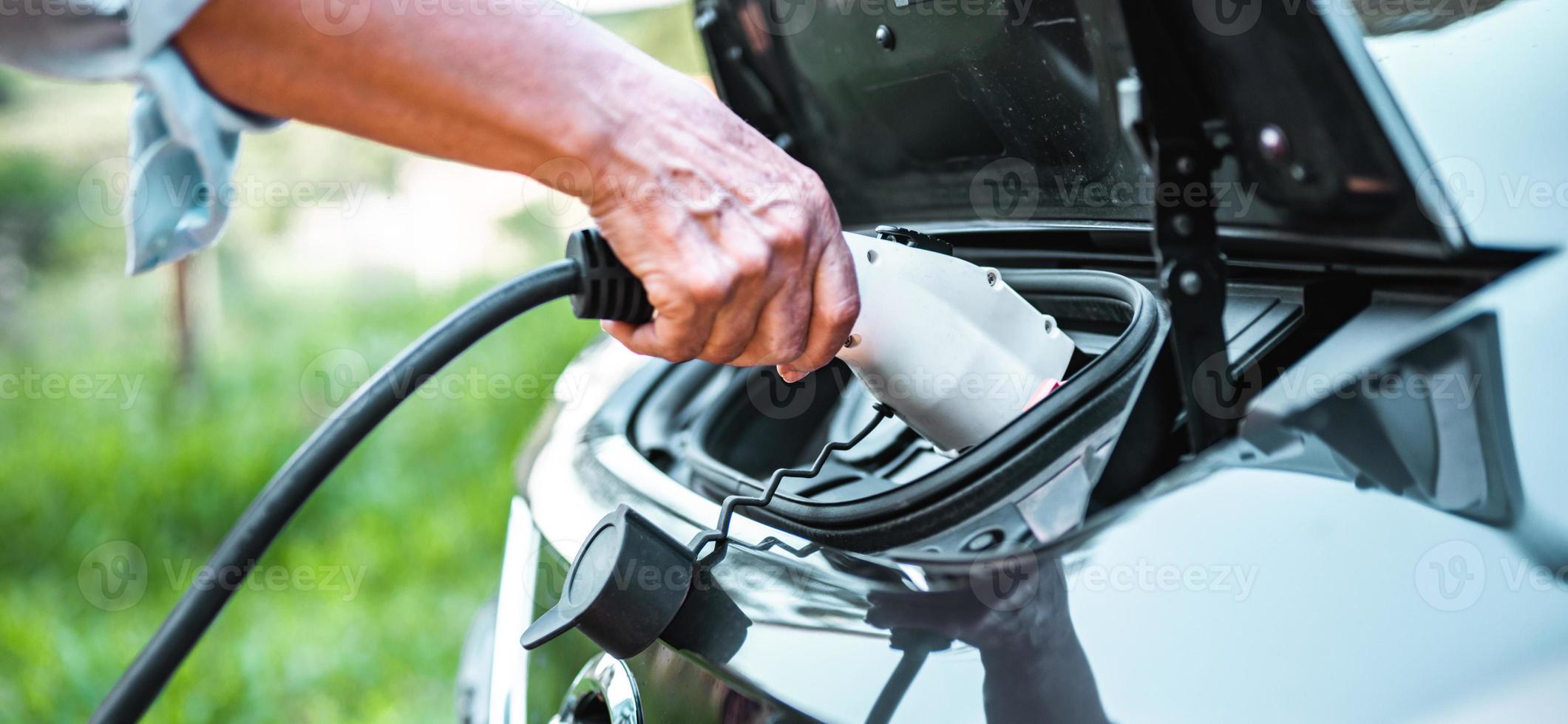 la mano humana sostiene la carga del automóvil eléctrico y se conecta al automóvil eléctrico foto