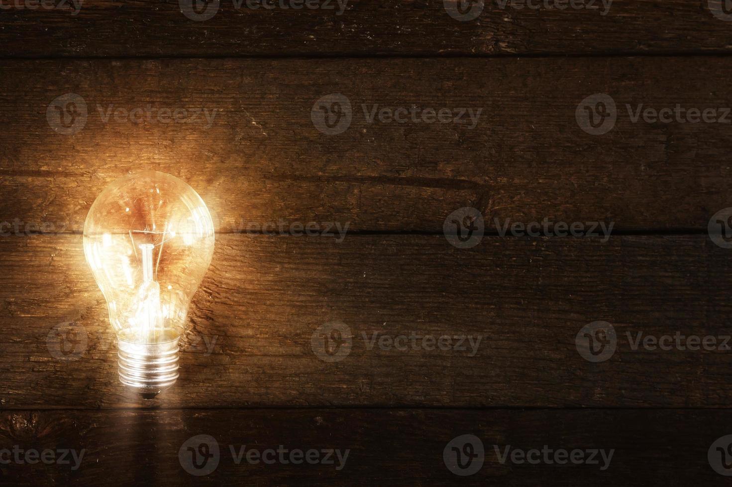 Glowing lightbulb on wooden background photo