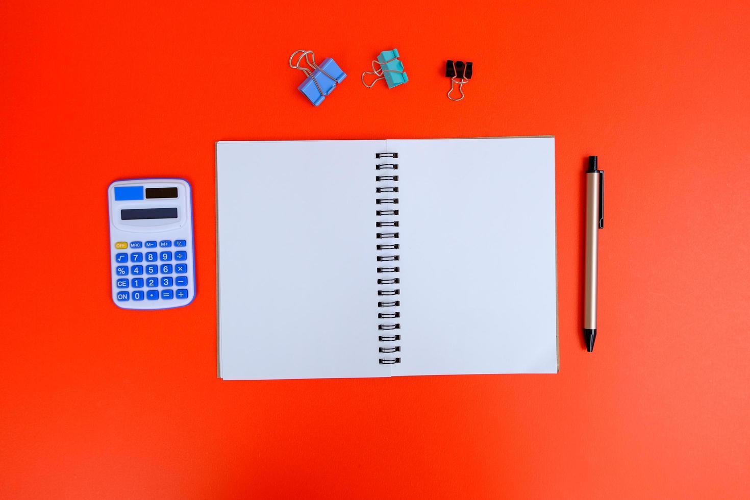 un cuaderno en blanco, un bolígrafo y anteojos están encima de una mesa de escritorio de oficina blanca. endecha plana, vista superior. mesa de escritorio de oficina de diseño blanco con computadora portátil, teléfono inteligente y suministros foto