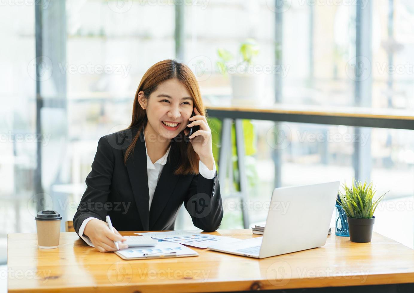 la mujer asiática con ropa informal es feliz y alegre mientras se comunica con su teléfono inteligente y trabaja en una oficina moderna. foto