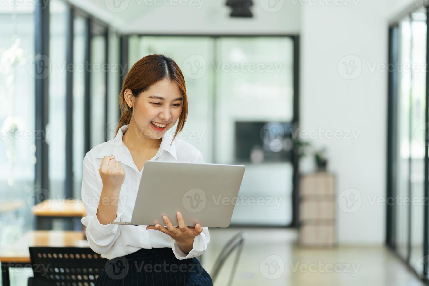 mujer joven con laptop expresando entusiasmo en la oficina en casa, mujer asiática emocionada se siente eufórica leyendo buenas noticias en línea. foto