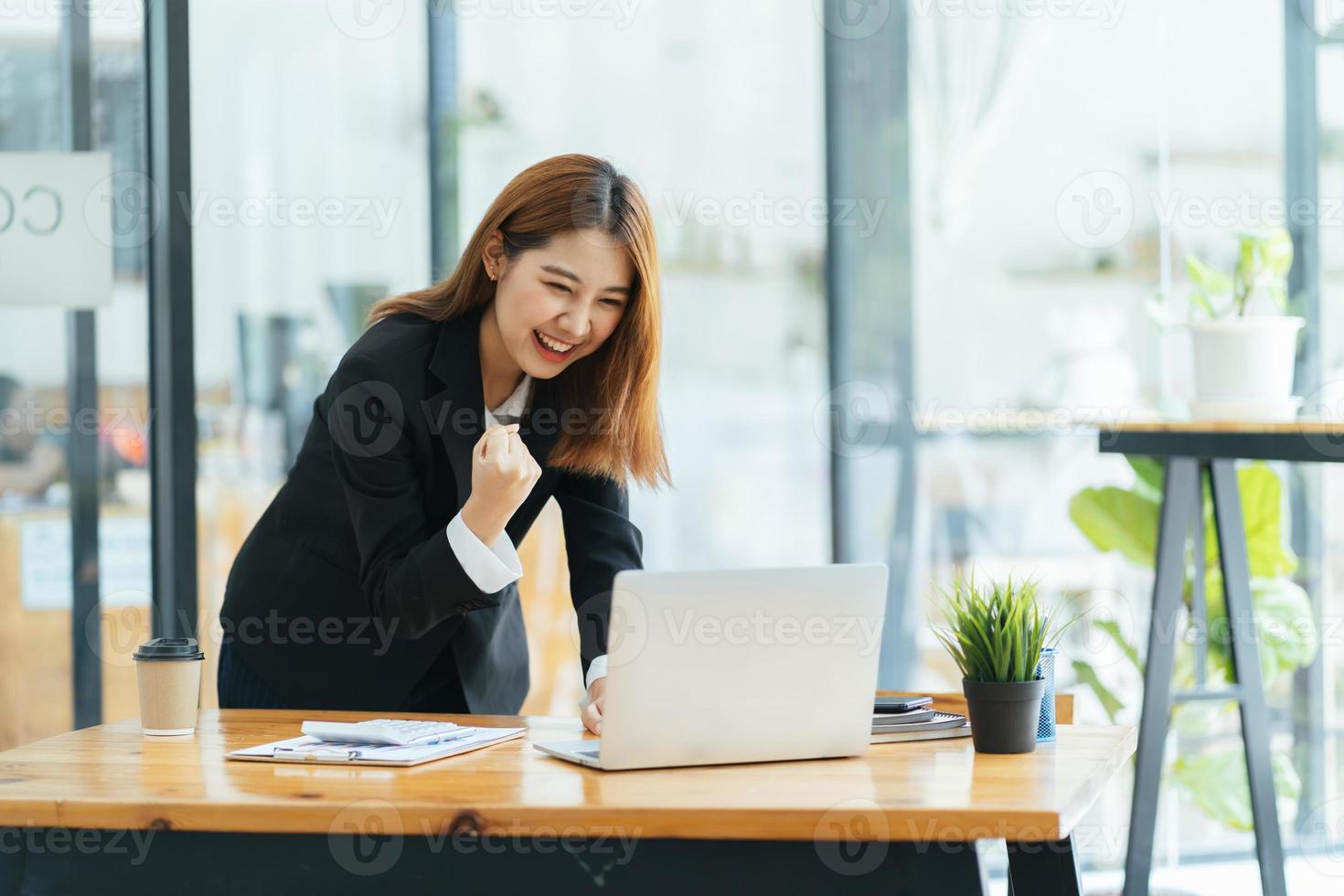 mujer joven con laptop expresando entusiasmo en la oficina en casa, mujer asiática emocionada se siente eufórica leyendo buenas noticias en línea. foto