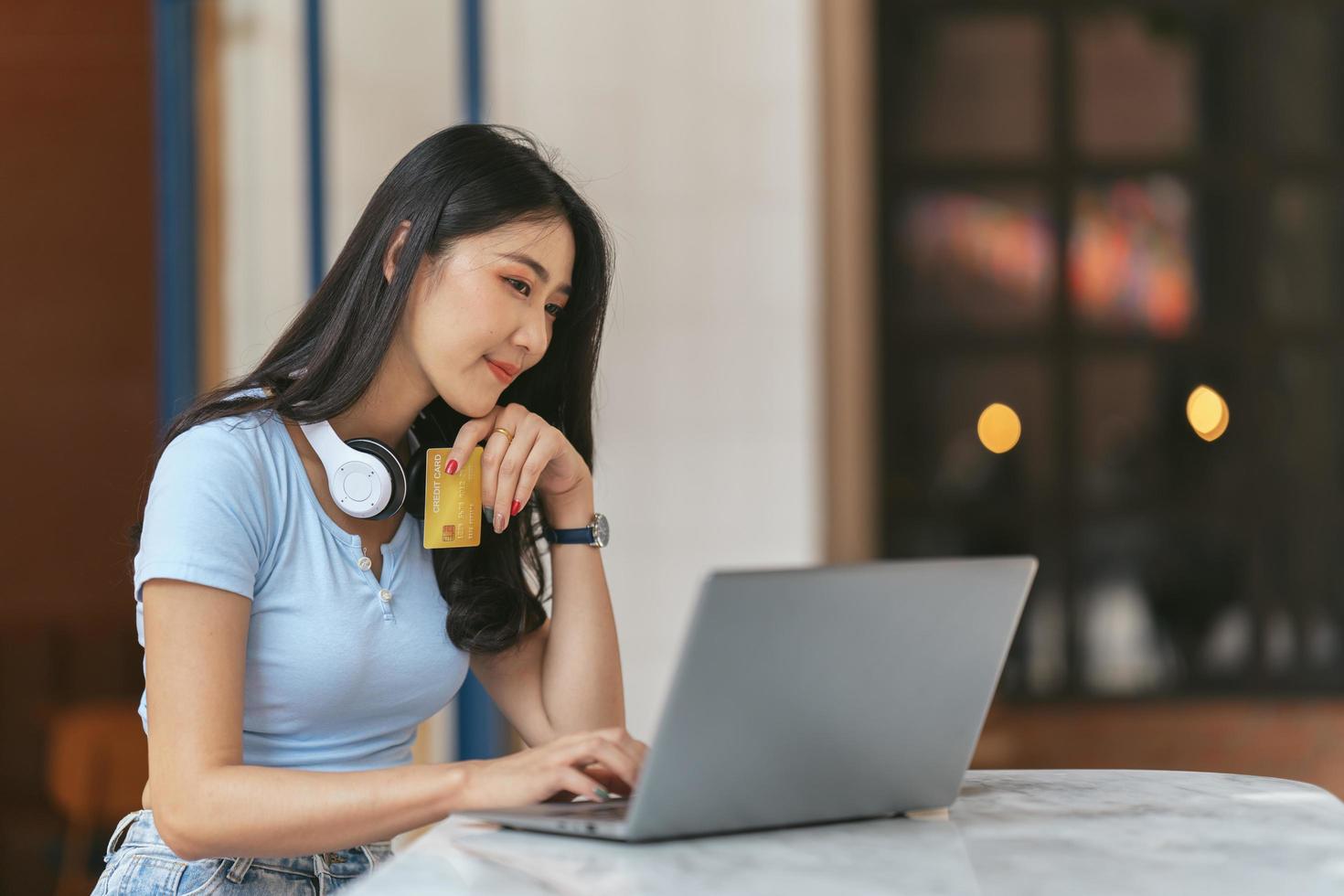 concepto de banca en línea. retrato de una joven asiática feliz con una laptop y una tarjeta de crédito sentada en un café, mujeres asiáticas sonrientes disfrutando de hacer pagos desde casa. foto