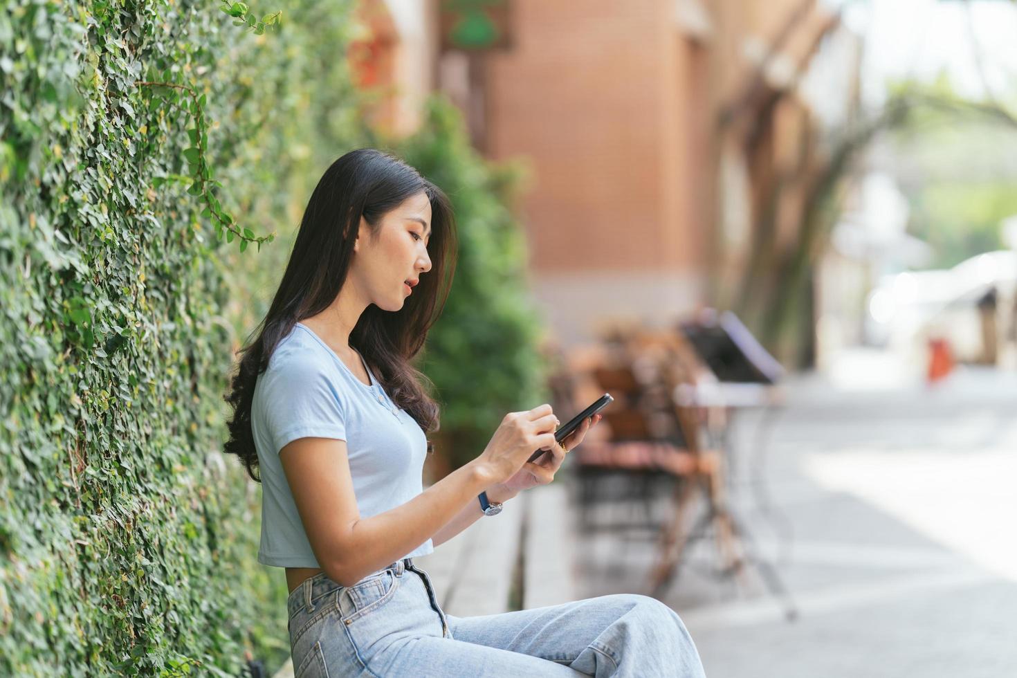 Happy asian woman smiling and holding cellphone while sitting in street summer cafe. photo