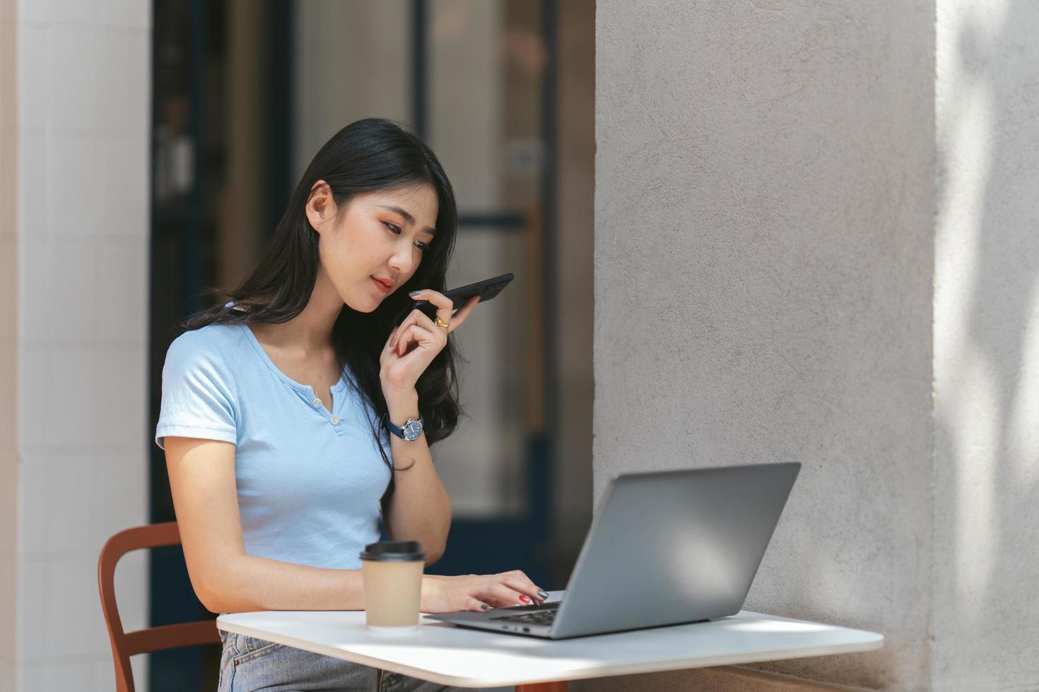 retrato de una hermosa mujer asiática sentada al aire libre en el restaurante de la cafetería durante el verano, usando una computadora portátil y un teléfono inteligente con tecnología inalámbrica inteligente, relajante descanso para tomar café en el restaurante de la cafetería. foto