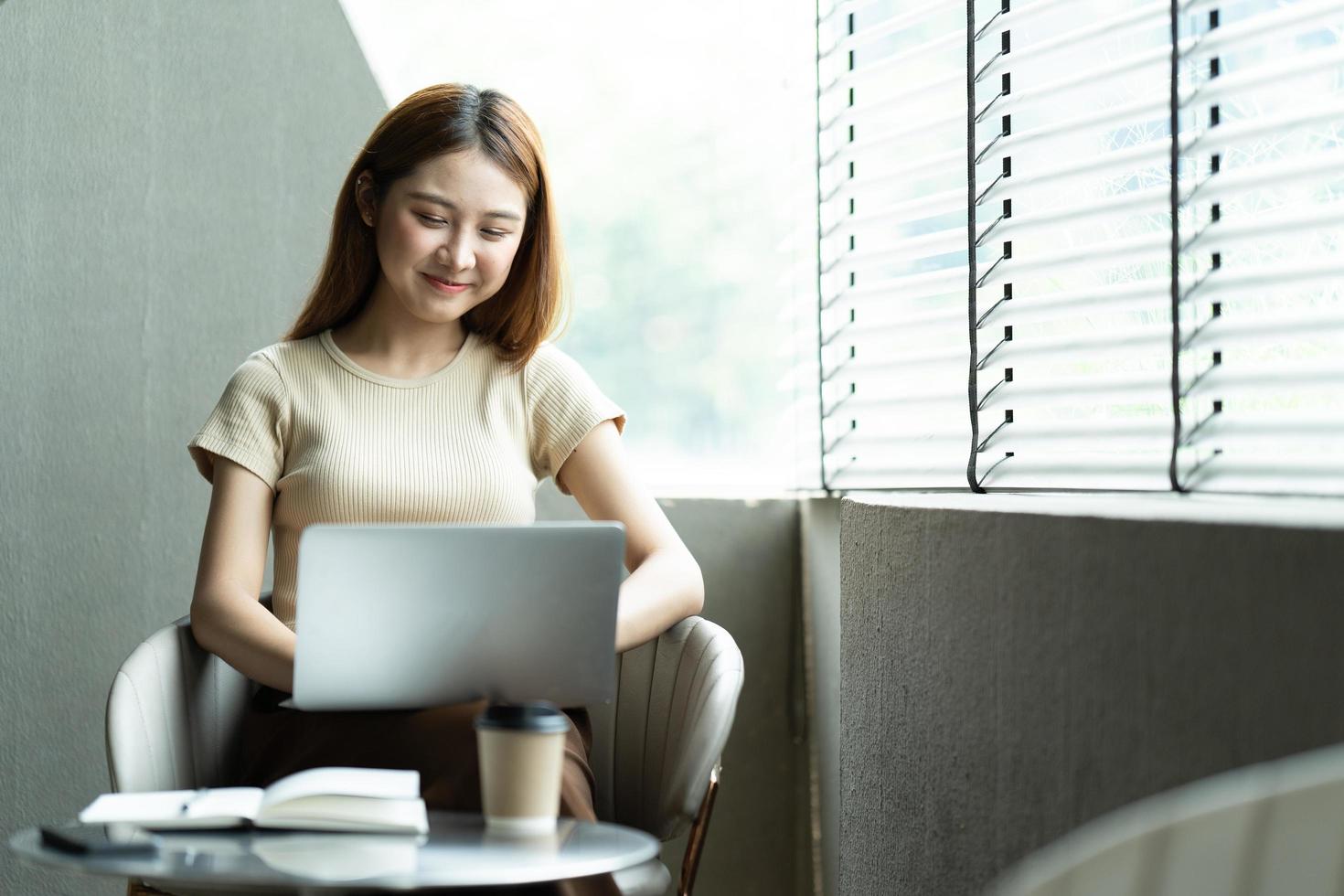 retrato de una hermosa mujer asiática sentada en el interior de un restaurante cafetería durante el verano, usando una computadora portátil y un teléfono inteligente con tecnología inalámbrica inteligente, relajándose en un café restaurante. foto