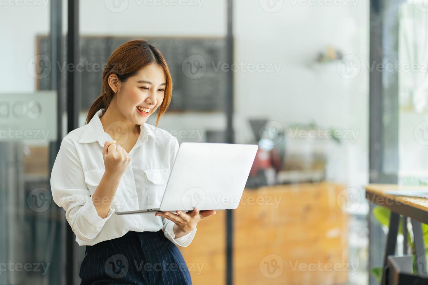 mujer joven con laptop expresando entusiasmo en la oficina en casa, mujer asiática emocionada se siente eufórica leyendo buenas noticias en línea. foto