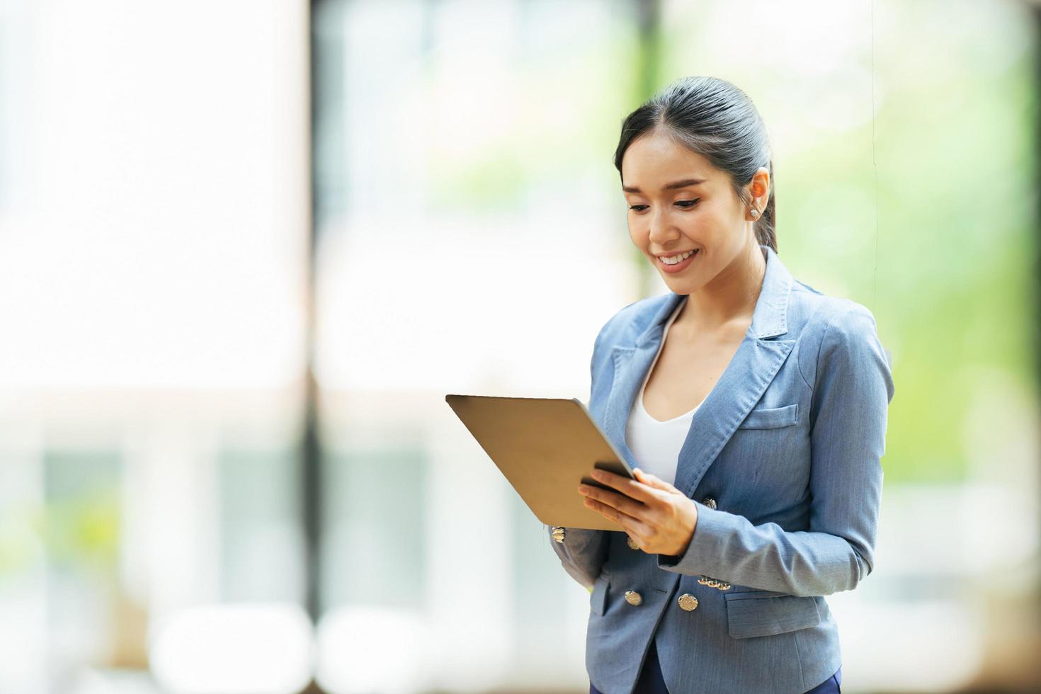 Asian woman with digital tablet standing in modern office background and copy space, Fashion business photo of beautiful girl in casual suit with tablet.