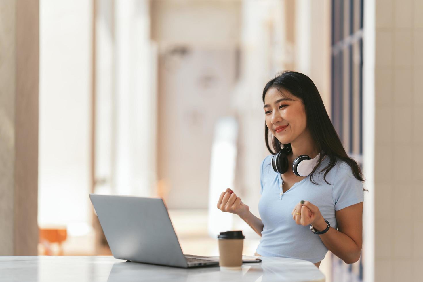 mujer joven con laptop expresando entusiasmo en la oficina en casa, mujer asiática emocionada se siente eufórica leyendo buenas noticias en línea. foto