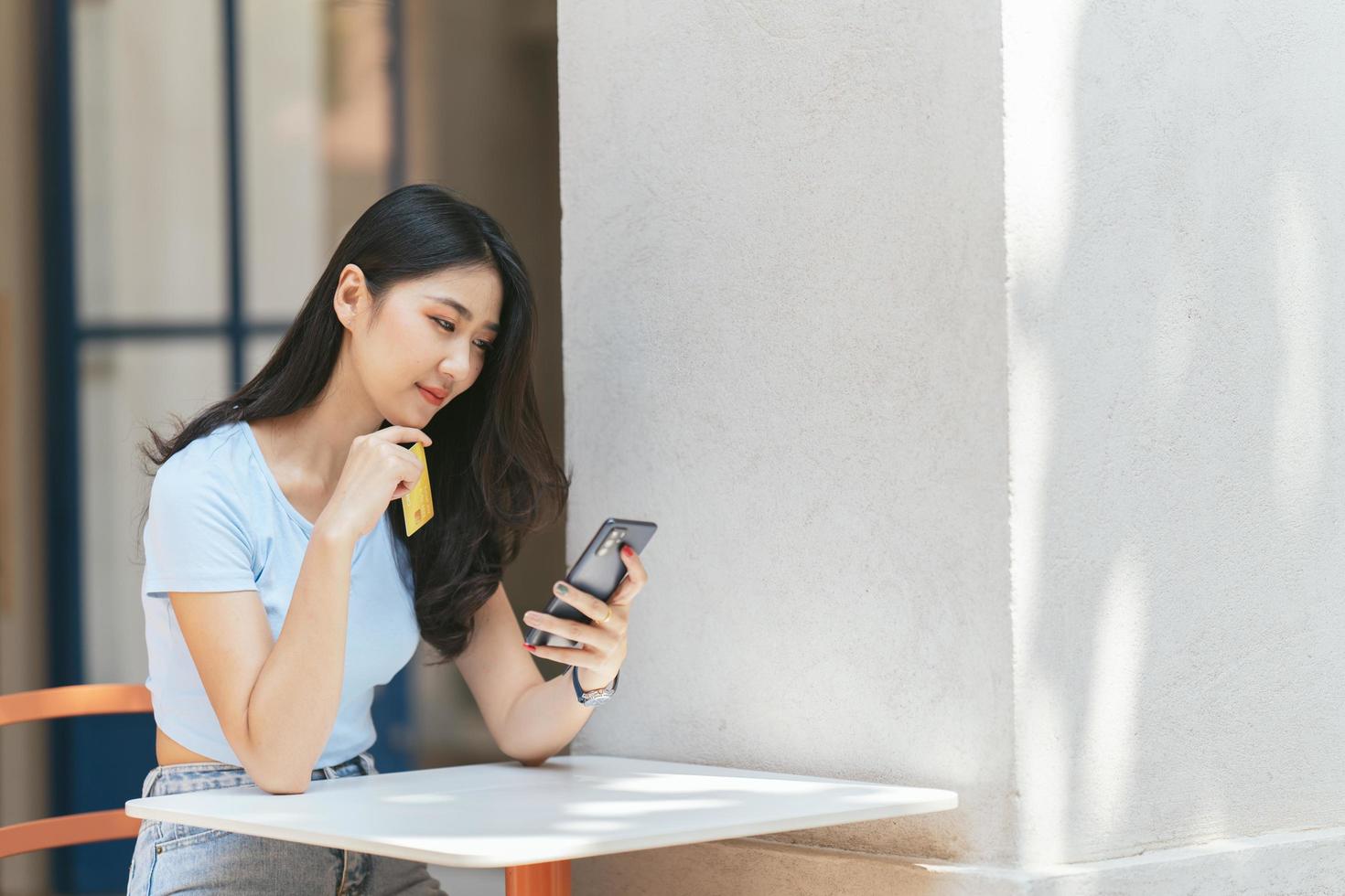 concepto de banca en línea. retrato de una joven asiática feliz con teléfono inteligente y tarjeta de crédito sentada en un café, mujeres asiáticas sonrientes disfrutando de hacer pagos desde casa. foto